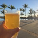 夕日を背景にビールを持つ手とプールサイドの風景