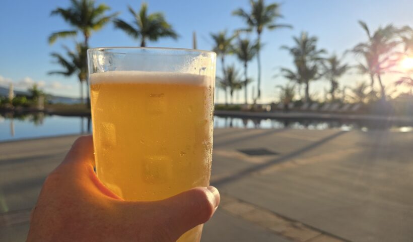 夕日を背景にビールを持つ手とプールサイドの風景