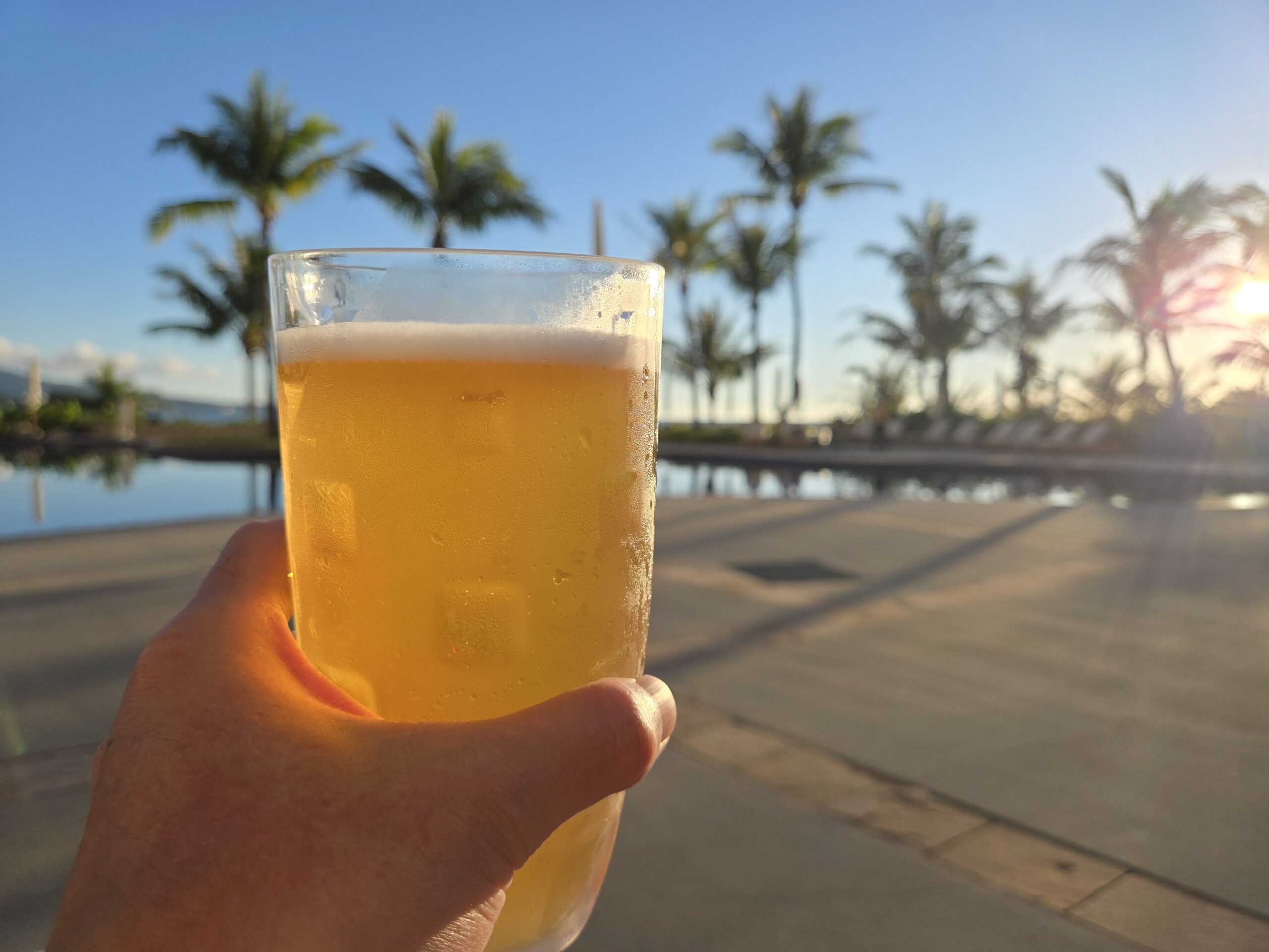 夕日を背景にビールを持つ手とプールサイドの風景