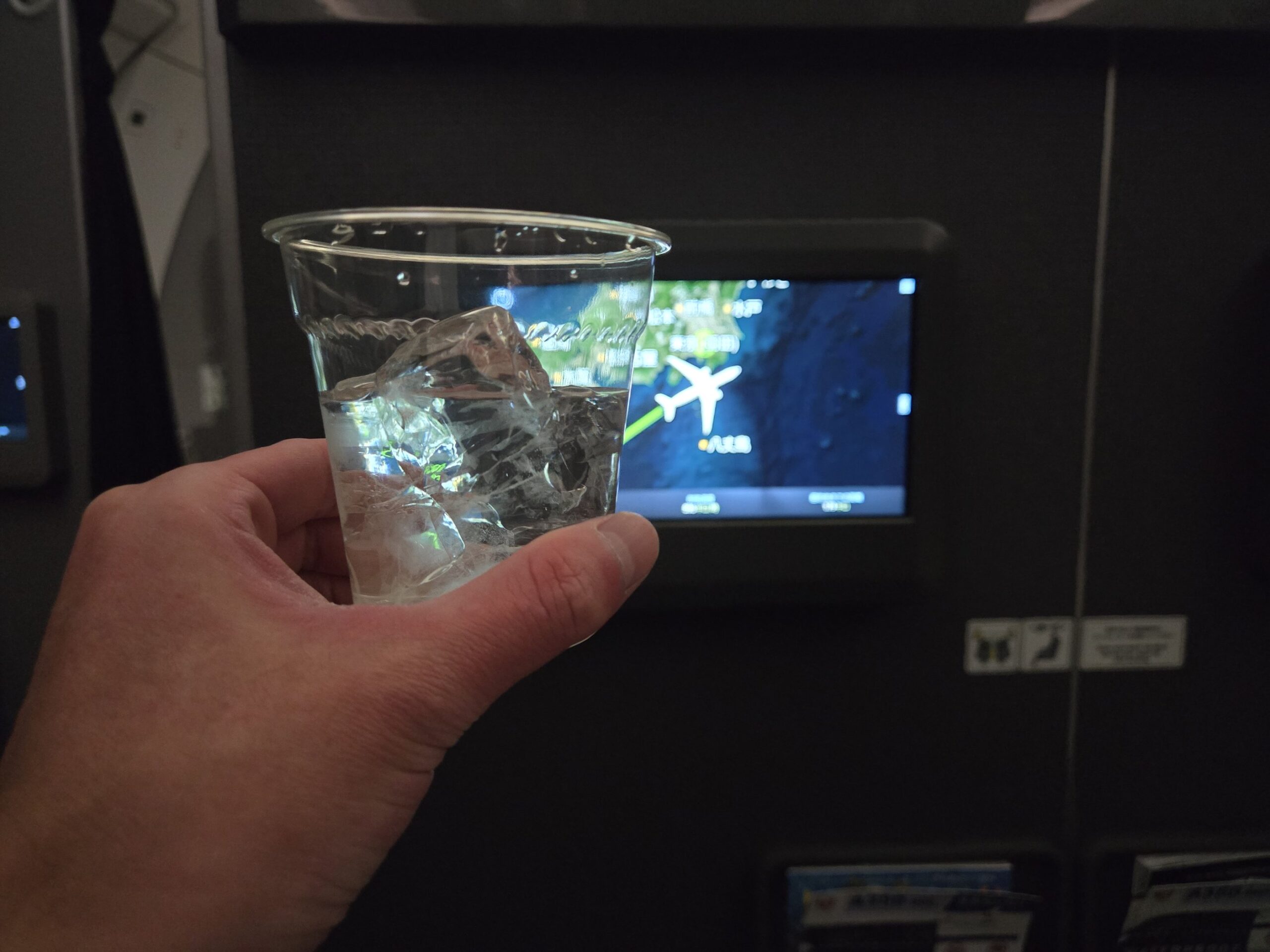透明カップの氷入りドリンクと機内スクリーン